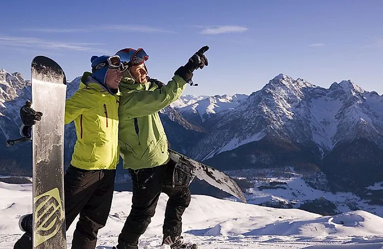 Zwei Snowboarder mit Blick auf die verschneiten Berge bei Scuol in der Schweiz