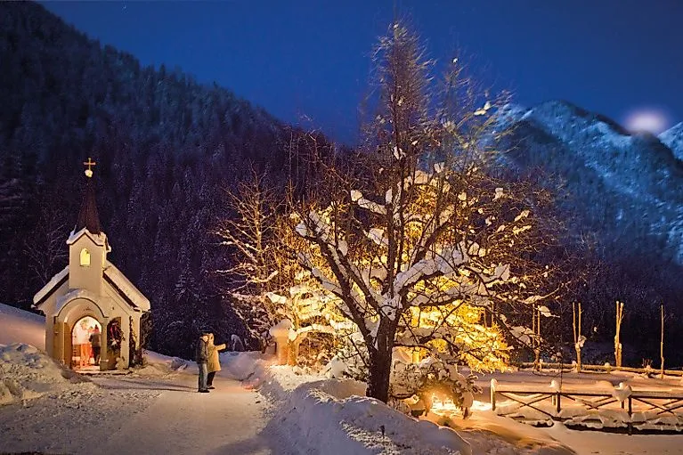 Stimmungsvolle Winteraufnahme einer beleuchteten Kapelle mit Weihnachtsbaum im Schnee bei Nacht in St. Johann im Pongau.