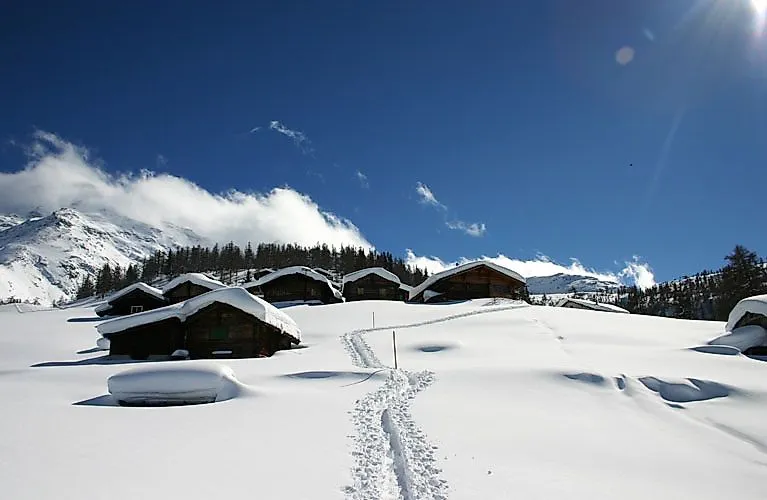 Verschneite Hüttenlandschaft in Fiesch-Aletsch mit tiefem Schnee und strahlend blauem Himmel