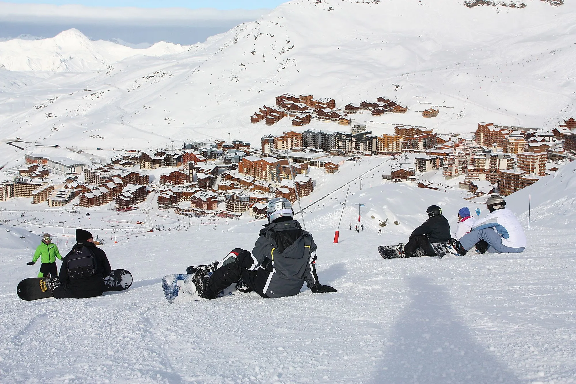 Snowboarder sitzen auf Piste mit Blick auf das Skidorf Formigal in den verschneiten Pyrenäen