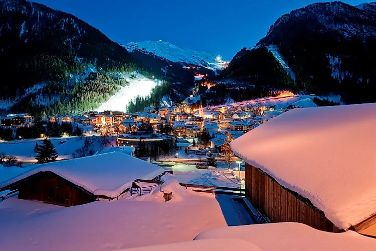 Winter evening view of illuminated Ischgl with glistening snow-covered roofs, pistes and atmospheric mountain scenery.