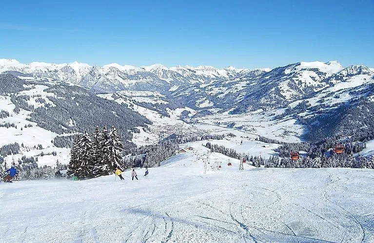 Wintersportler auf einer weiten Skipiste in Zweisimmen mit verschneiten Gipfeln im Hintergrund.