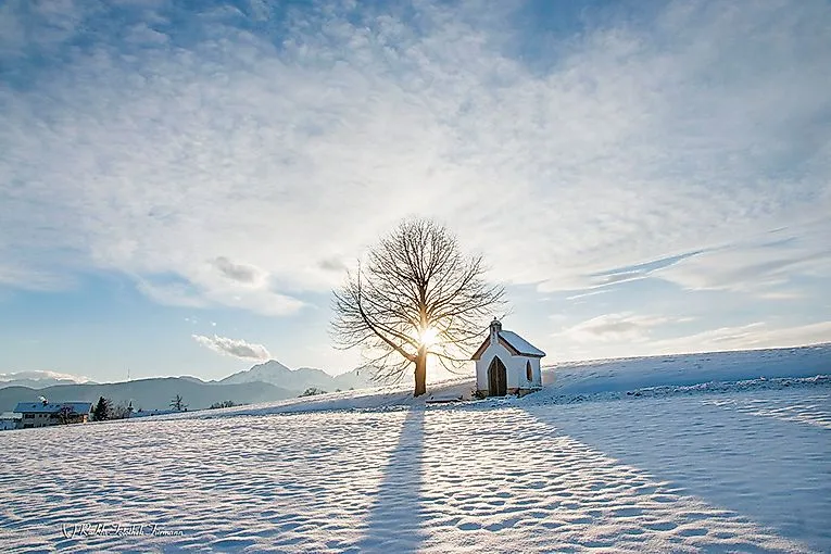 Verschneite Winterlandschaft in Anger mit Kapelle, Baum und tiefstehender Sonne