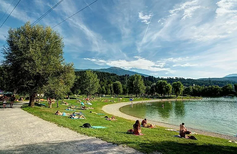 Menschen genießen einen warmen Sommertag am Baggersee in Innsbruck, umgeben von üppigem Grün und Bergen im Hintergrund.