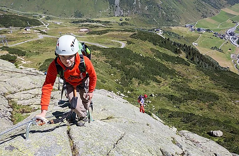 Kletterer erklimmt mit Sicherung einen Felsen in Galtür, mit Blick ins grüne Paznauntal.