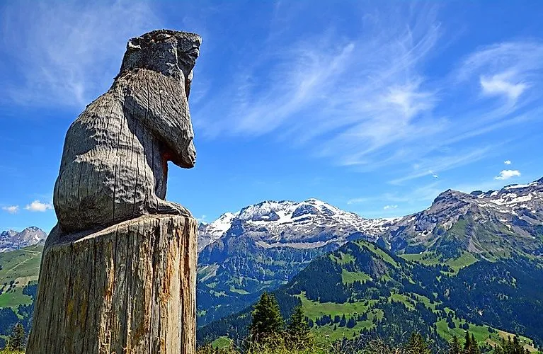 Holz-Murmeltier vor sommerlicher Bergkulisse bei Lenk im Simmental in der Schweiz