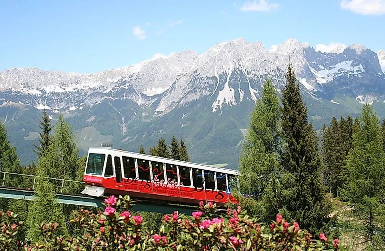 Rote Panoramabahn fährt im Sommer vor beeindruckender Bergkulisse am Wilden Kaiser.