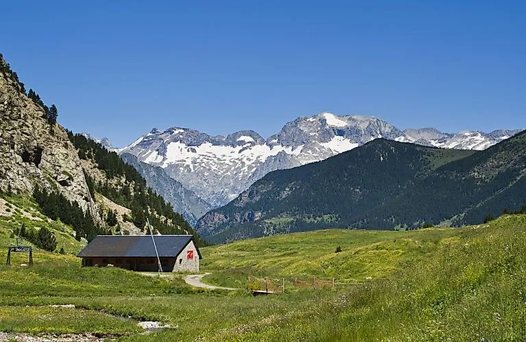 Sommerliche Berglandschaft bei Cerler mit grünen Wiesen, Almhütte und Blick auf schneebedeckte Pyrenäengipfel