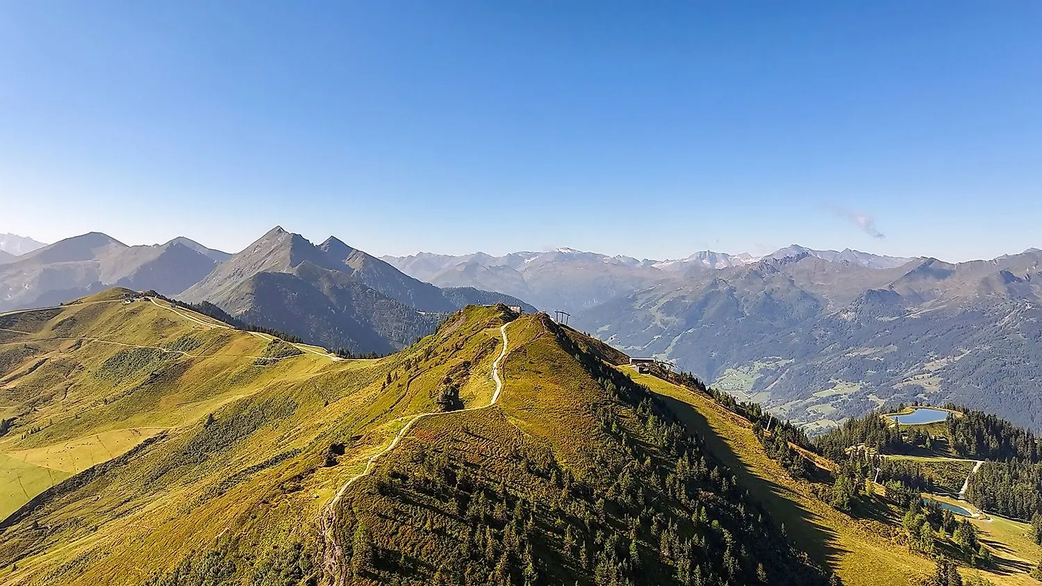 FlyingCam Luftaufnahme der grünen Bergrücken von Dorfgastein mit Fernsicht auf die Hohen Tauern im Sommer.