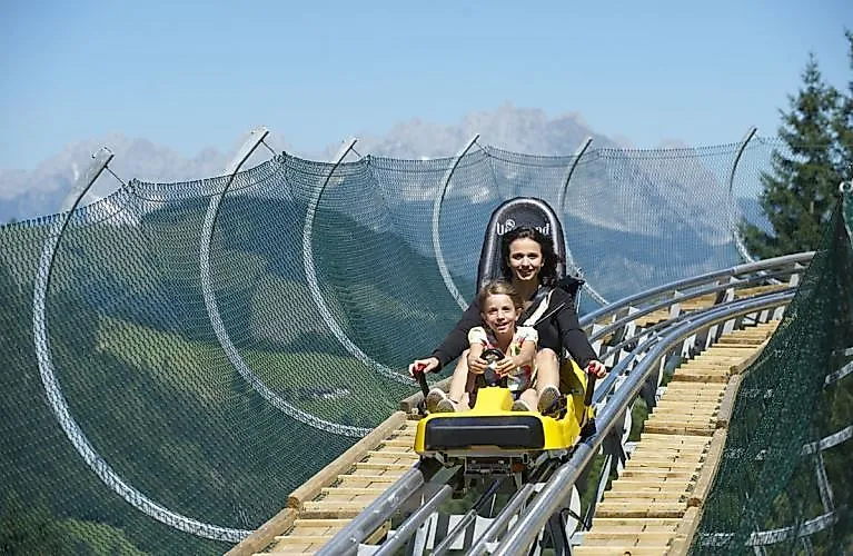 Mutter und Kind fahren lachend mit Timoks Coaster durch die Sommerlandschaft in Fieberbrunn.