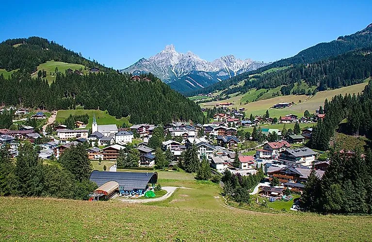 Blick auf den idyllischen Ort Filzmoos in den Salzburger Alpen, eingebettet zwischen grünen Hügeln mit dem markanten Dachsteinmassiv im Hintergrund.