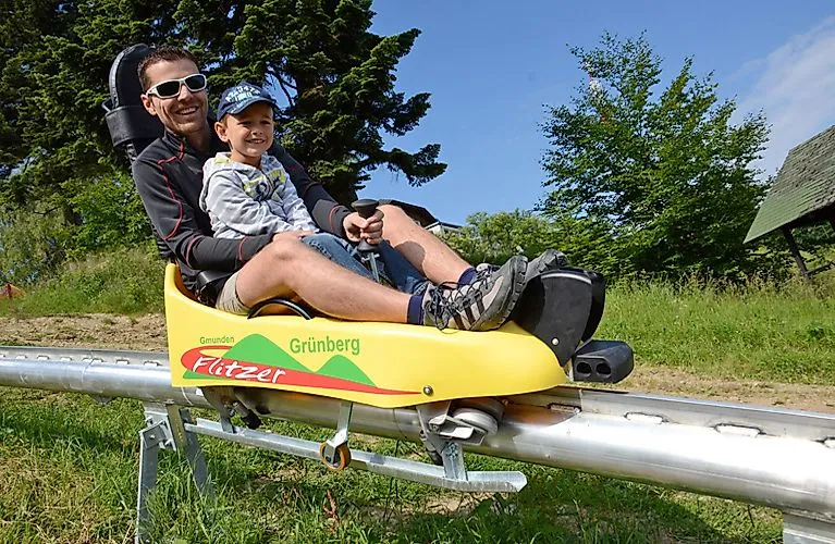 Vater und Sohn fahren lachend mit der Sommerrodelbahn Grünberg in Gmunden.