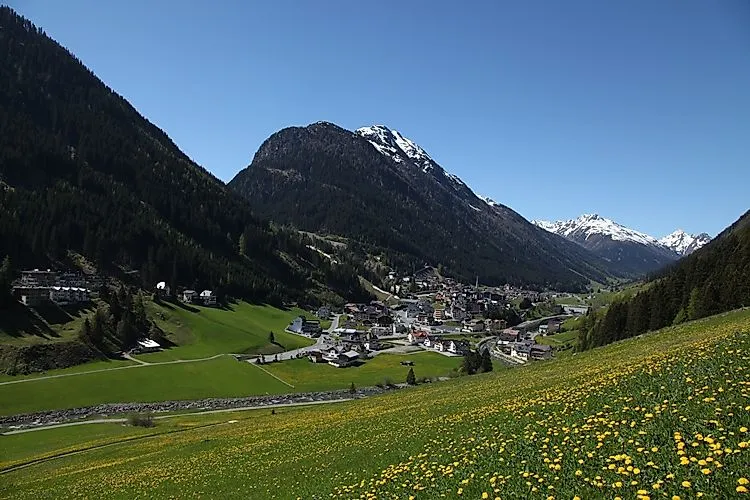 View over the sunny Paznaun valley to the Tyrolean vacation resort of Ischgl, nestled between lush green mountain slopes and snow-capped peaks.