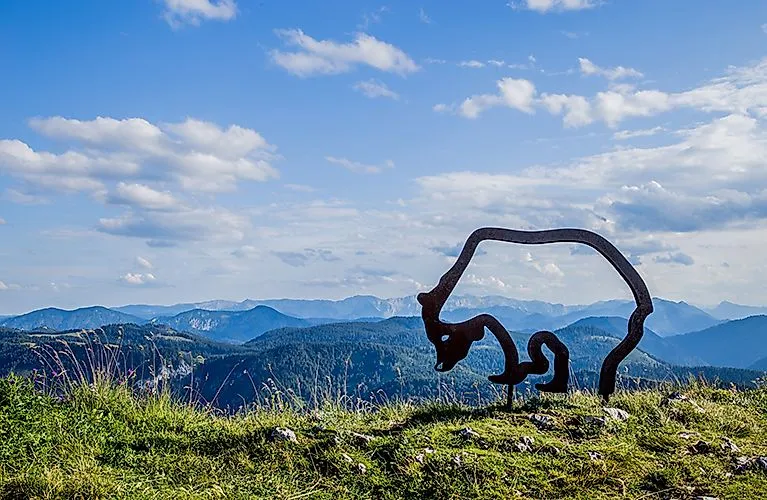Sommerliches Panorama bei Lackenhof am Ötscher mit moderner Skulptur und Blick auf bewaldete Hügel und Berge unter blauem Himmel.