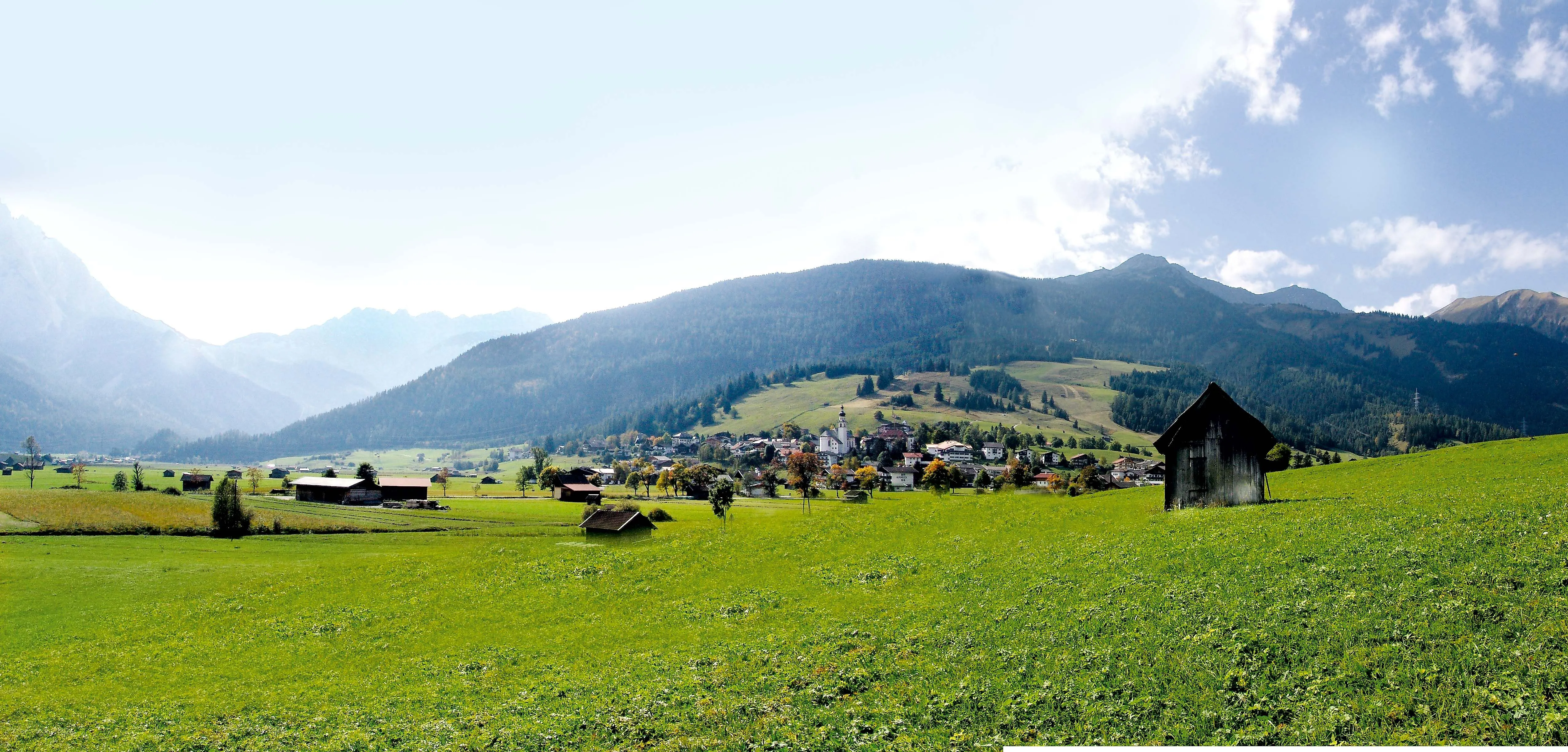Sommerliche Aussicht auf das Dorf Lermoos in Tirol mit grünen Wiesen, Bergen im Hintergrund und traditioneller Alpenidylle.