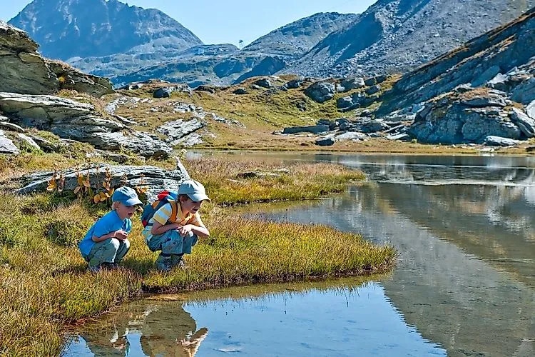 Zwei Kinder entdecken einen klaren Bergsee in alpiner Sommerlandschaft