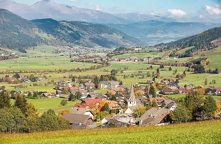 Weitblick über die grüne Landschaft von St. Margarethen im Lungau mit verstreuten Häusern, Feldern und Bergen im Hintergrund.
