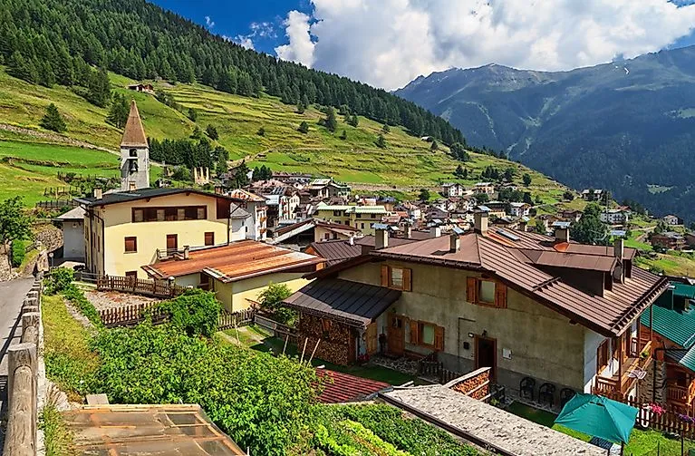 Vista di Pejo in estate con la chiesa, il paese di montagna e il paesaggio verde a terrazze in Val di Sole