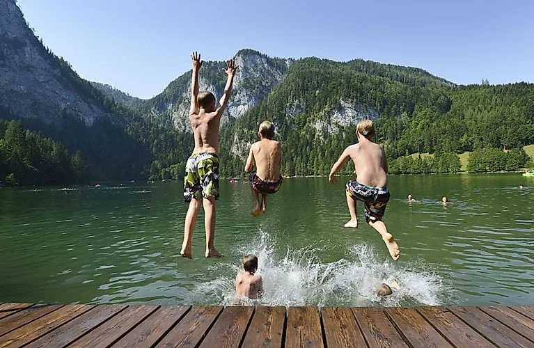 Kinder springen lachend in einen klaren Bergsee bei Windischgarsten an einem Sommertag.