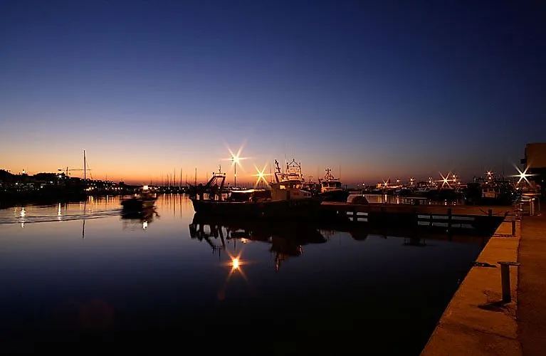 Fischerboote im Hafen von Cambrils bei Sonnenaufgang mit ruhigem Wasser und funkelnden Lichtern am Morgenhimmel