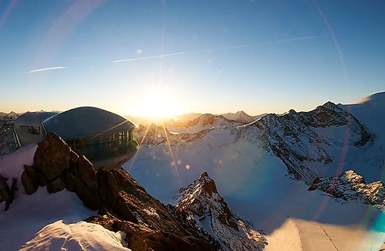 Sonnenaufgang über dem Pitztaler Gletscher mit futuristischer Bergstation in verschneiter Hochgebirgslandschaft