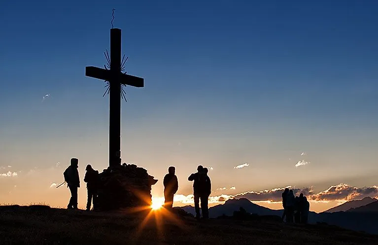 Wanderer erleben den Sonnenaufgang am Gipfelkreuz in Serfaus-Fiss-Ladis.