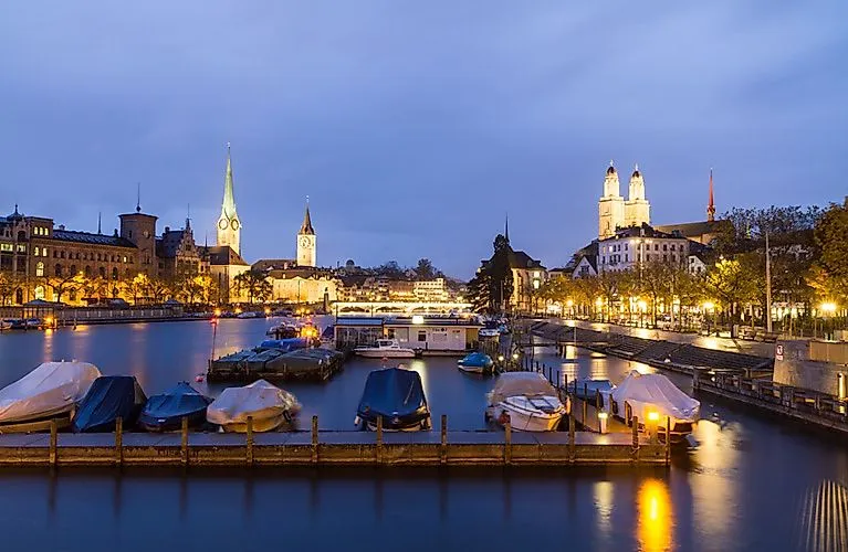 Abendliche Panoramaaufnahme von Zürich mit beleuchteter Altstadt, Fraumünster und Großmünster am Zürichsee.