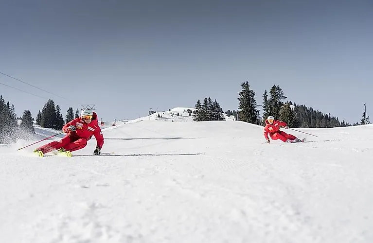 Zwei Skilehrer in roten Anzügen bei einer rasanten Abfahrt auf perfekt präparierter Piste in Zweisimmen.